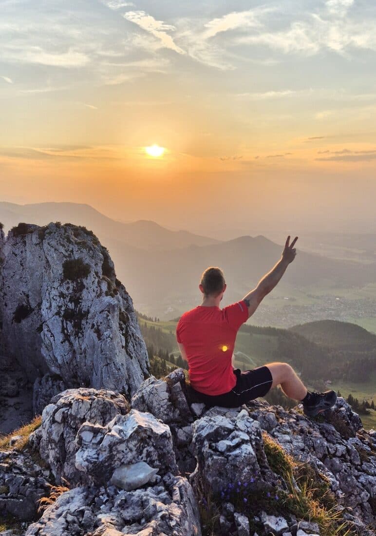 Dietmar Kühnel sitzt bei Sonnenuntergang auf einem Berggipfel über dem Voralpenland.